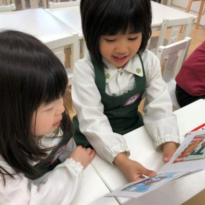 図書室で本を読んでいる二人の女の子。彼らは学校の制服を着ており、本に夢中になっている様子が見て取れます。