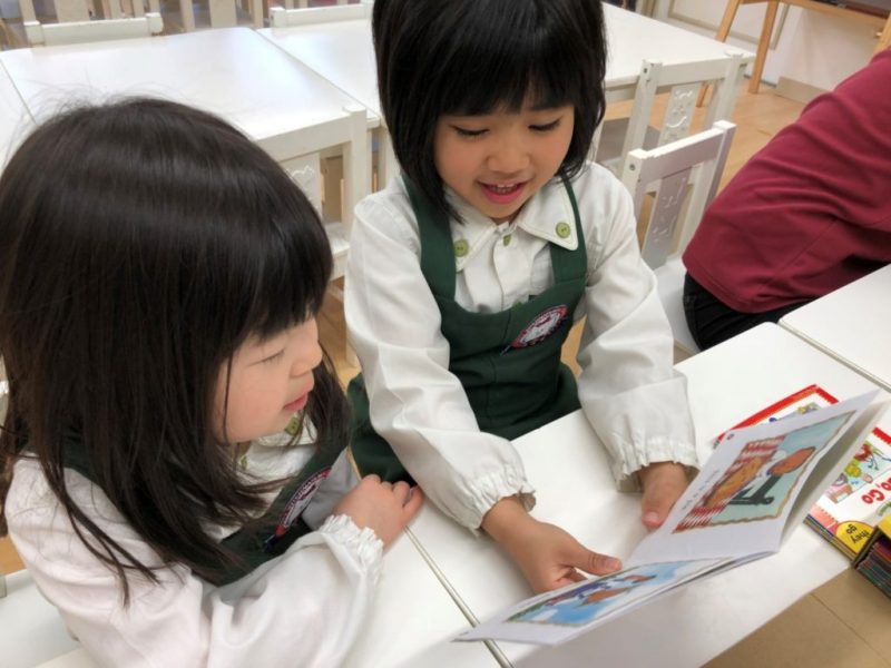 図書室で本を読んでいる二人の女の子。彼らは学校の制服を着ており、本に夢中になっている様子が見て取れます。